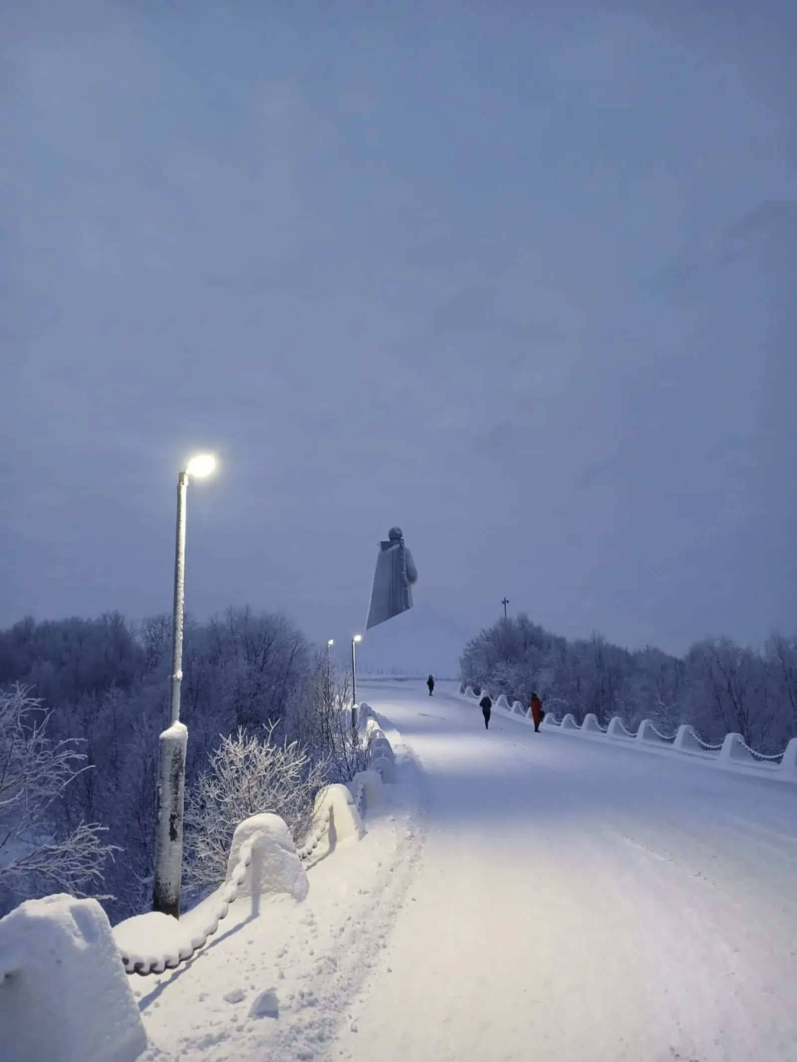 Snow-covered path leading uphill beneath streetlights at dusk