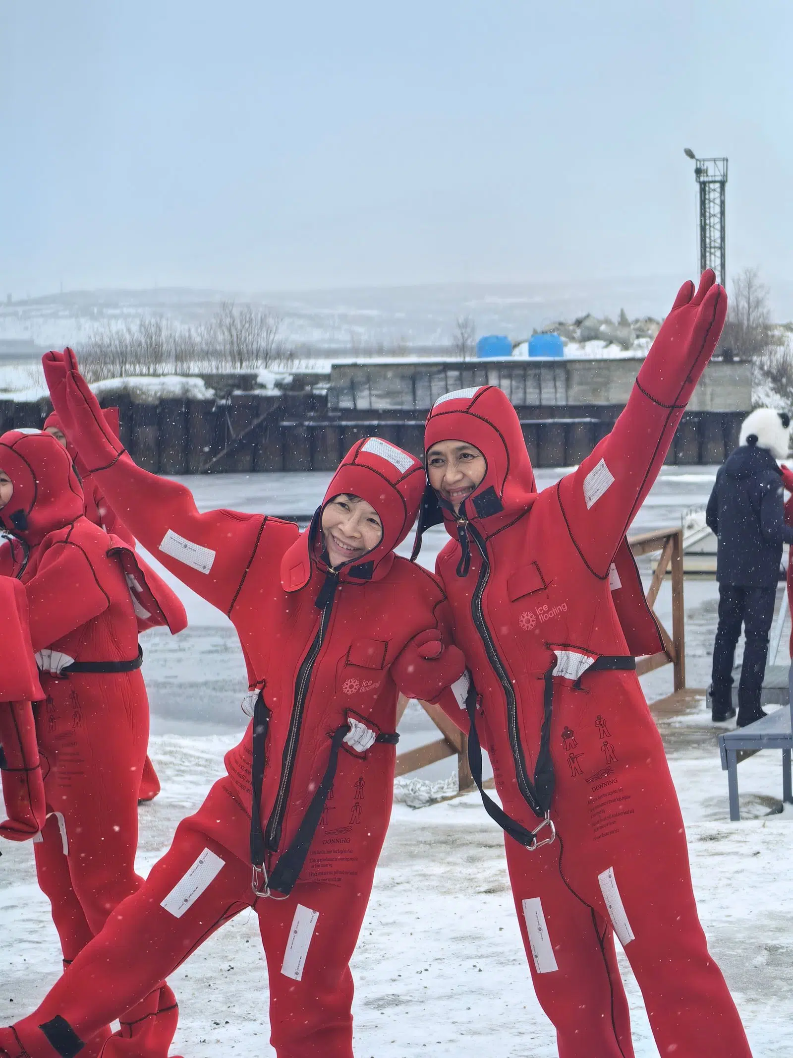 Three travelers posing in red immersion suits at the snowy bay