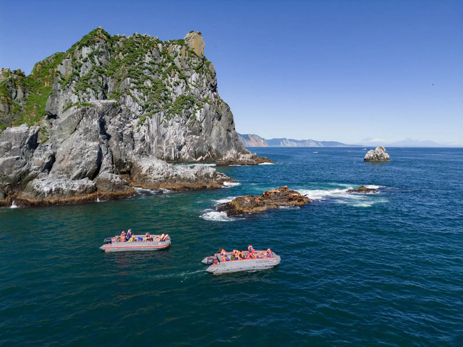 Two inflatable boats passing a green rocky island