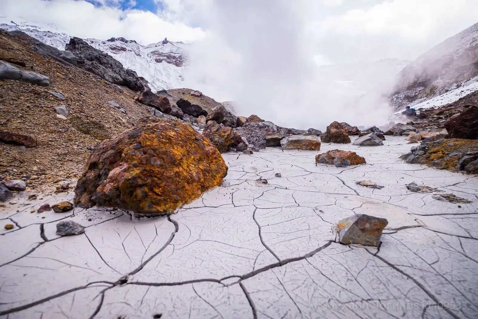 Steam rising between mineral-stained rocks in a geothermal valley