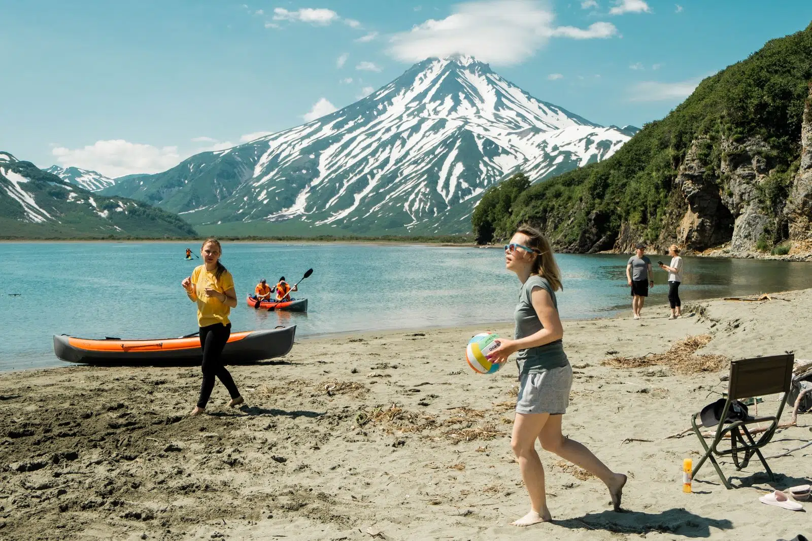 Travelers beside a canoe on a black-sand beach below a volcano