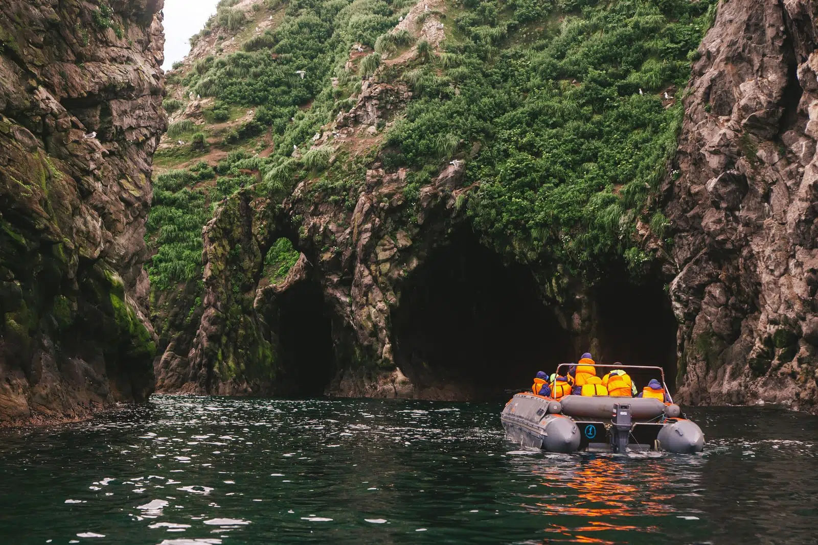 Travelers in an inflatable boat entering a narrow sea grotto