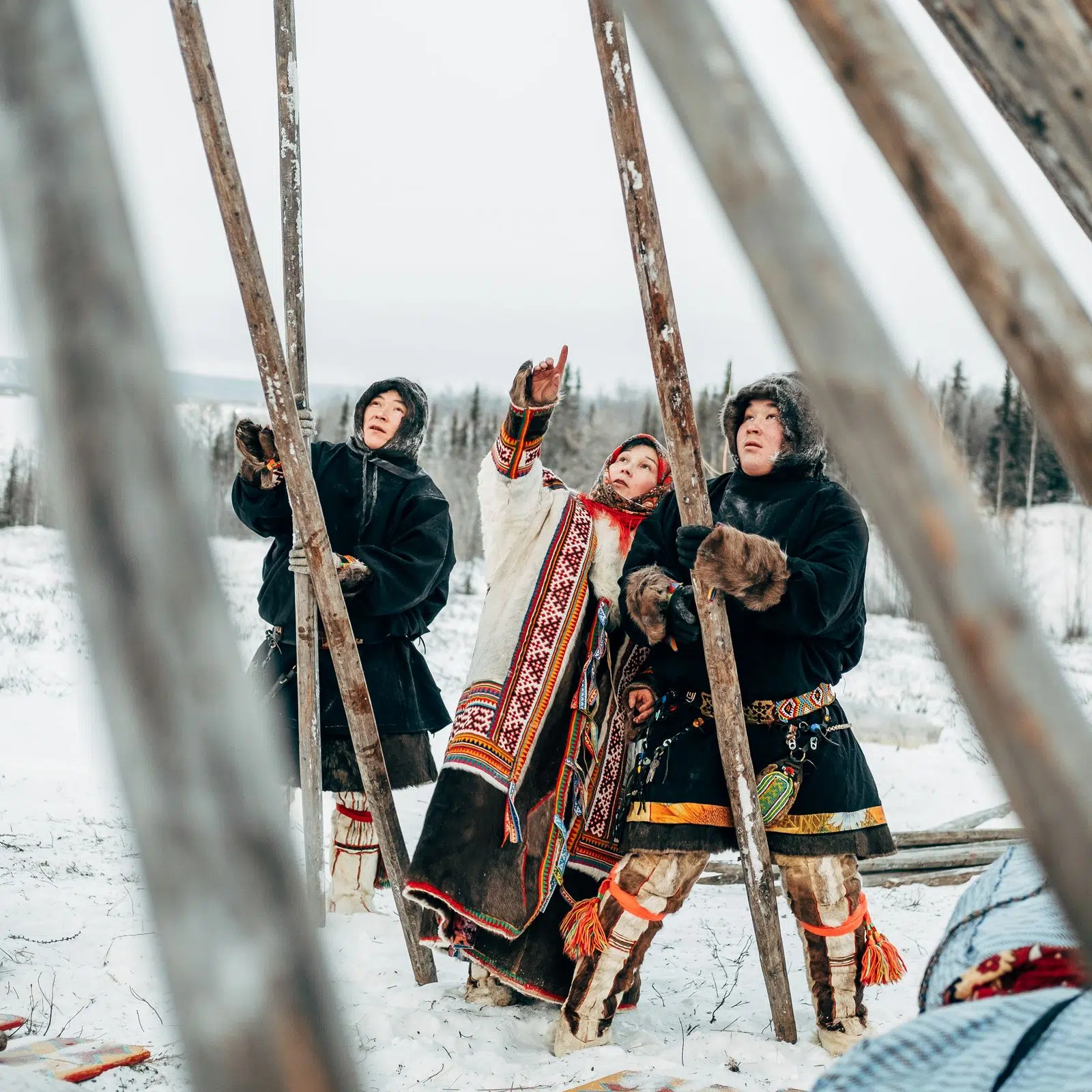 Nenets hosts in traditional clothing standing with long wooden poles