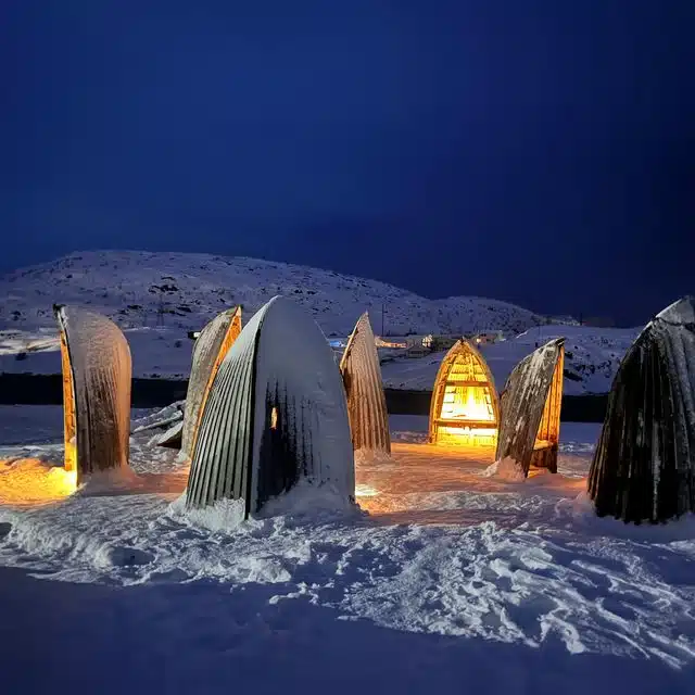 Illuminated whale-tail sculptures beside a snowy Arctic bay