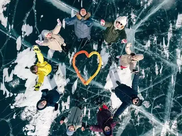 Travelers lying around a heart shape on clear lake ice
