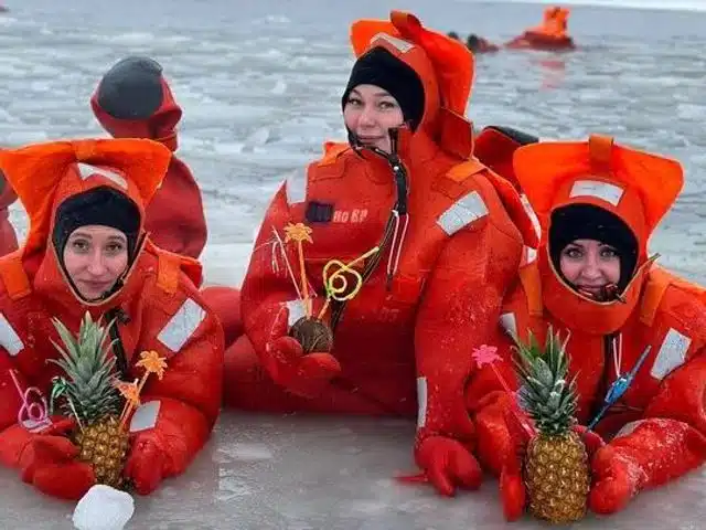 Ice-floating participants posing on the snowy shore with pineapples