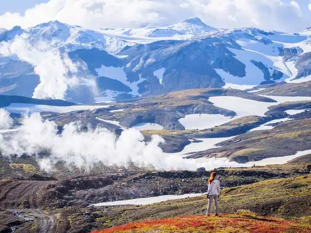 A traveler looking across a broad steaming geothermal valley