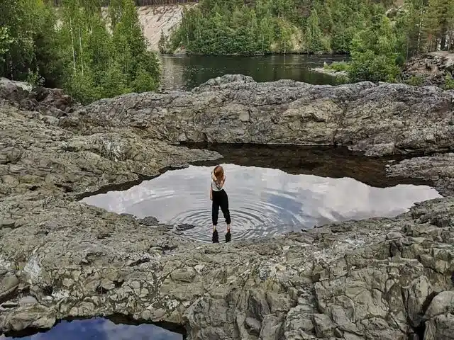 Traveler standing among rainwater pools on smooth Karelian rock