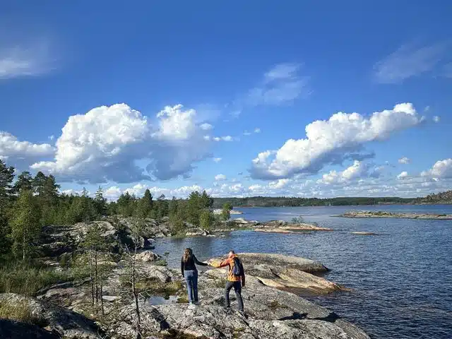 Travelers walking across a broad rocky shore beside a blue lake