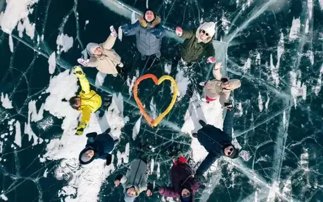 Travelers lying around a heart shape on clear lake ice