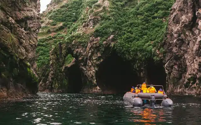 Travelers in an inflatable boat entering a narrow sea grotto